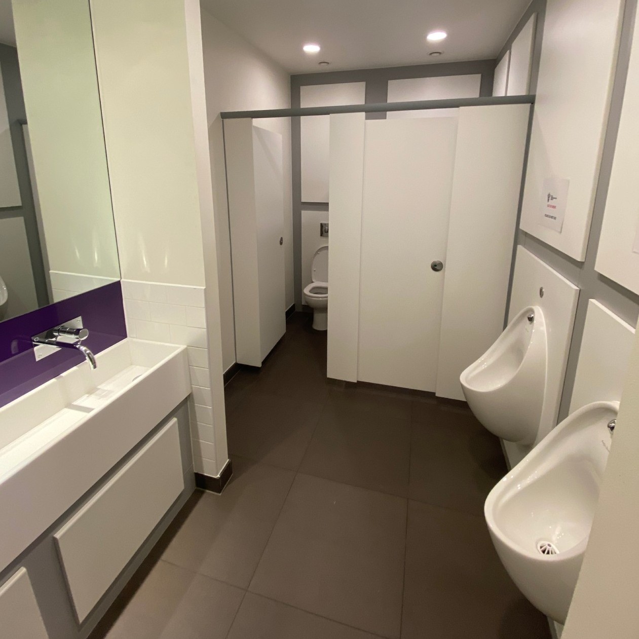 View of Men's toilet including cubicles urinals, mirror and sinks